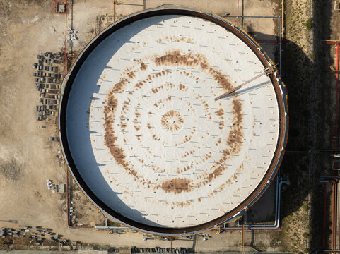 Aerial view of a large circular industrial storage tank with a white roof and concentric patterns at a refinery in Priolo Gargallo, Sicily, Italy.