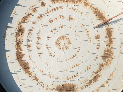 Aerial view of the circular roof of an industrial storage tank with geometric patterns and weathering stains in Priolo Gargallo, Sicily, Italy.