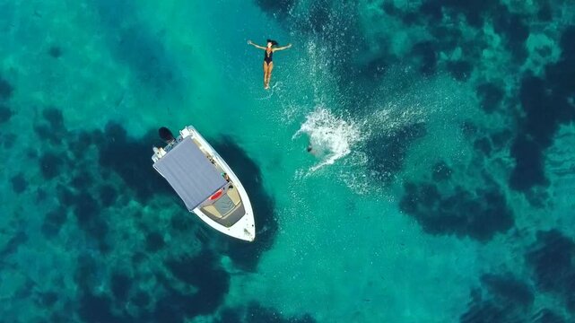 Aerial top down slow motion of a couple jumping off a boat into crystal clear turquoise water, summer fun and travel lifestyle