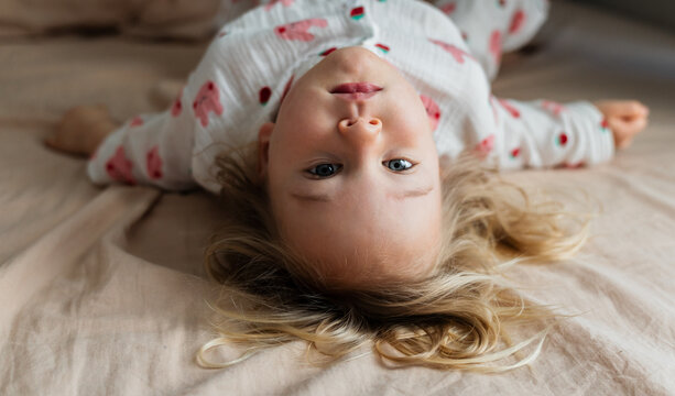 Toddler girl lying upside down on bed at home