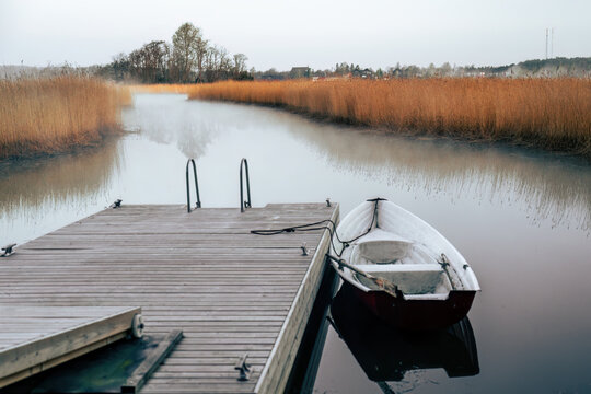 Small rowing boat moored at wooden pier on misty river morning