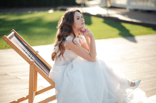 Bride in white dress relaxing on a deck chair outdoors in sunlight
