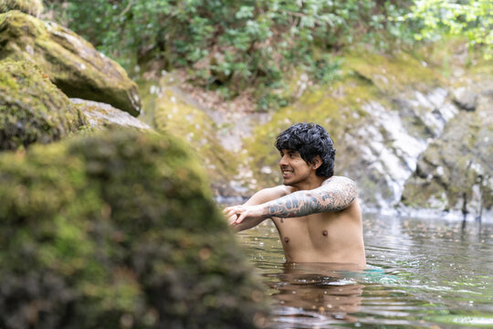 Tattooed man enjoying wild swimming in natural river
