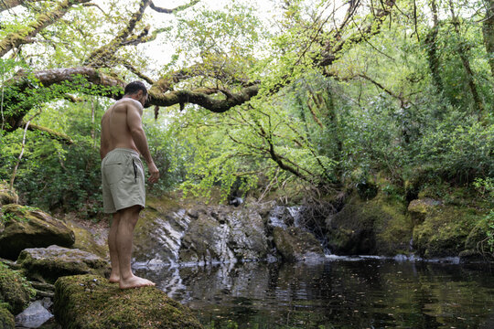 Man standing by a forest pond preparing for a swim