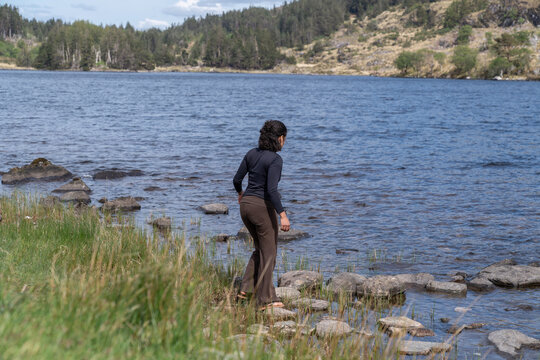 Woman hiking lakeside stepping on rocks enjoying nature