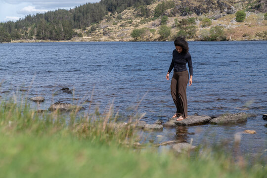 Woman stepping on rocks in serene lake landscape