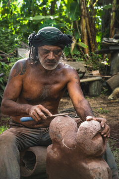 Tattooed Polynesian man carves a stone tiki sculpture