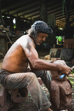 Tattooed artisan carves a wood sculpture outdoors