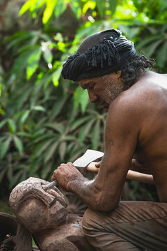 Elderly craftsman carves a stone figure outdoors