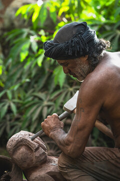 Mature artisan carving a stone statue outdoors