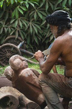 Elderly artisan carving a wooden sculpture outdoors