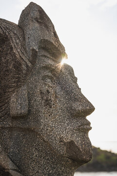 Sun flares behind a large stone face sculpture