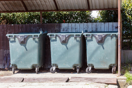 Three green wheeled trash bins stand in a row