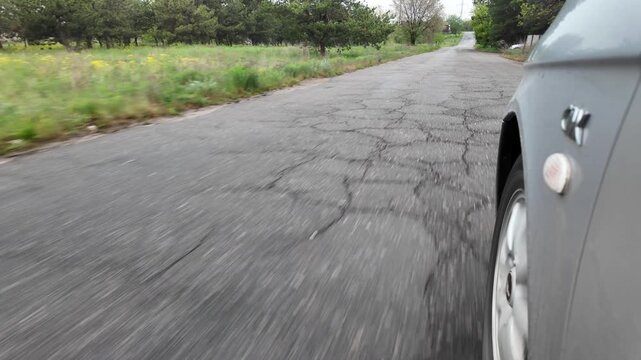 Slow-motion video shot from a moving silver car's perspective on a bumpy asphalt road in the countryside. The car's body 