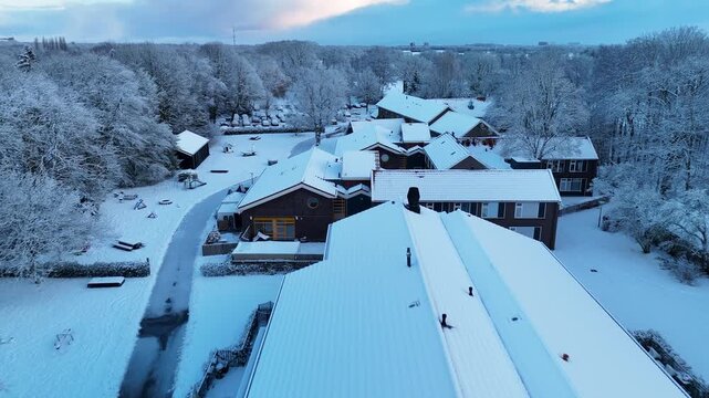 High-quality 4K aerial drone footage of a snow-covered housing estate inside a forest in the Netherlands. Calm winter sunrise, quiet atmosphere and beautiful snowy architecture.