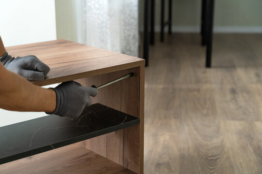 Hands of furniture assembler assemble wooden nightstand using screwdriver. Process of assembling furniture