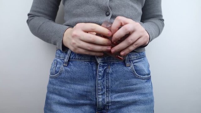 Close-up of a woman suffering from menstrual cramps holding her belly, with painkillers in her jeans pocket. Female health, period pain relief, and abdominal ache concept.