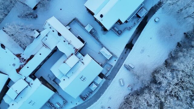 Cinematic 4K drone footage flying over a snowy residential complex surrounded by forest in the Netherlands during winter morning. Peaceful atmosphere and snow-covered buildings.