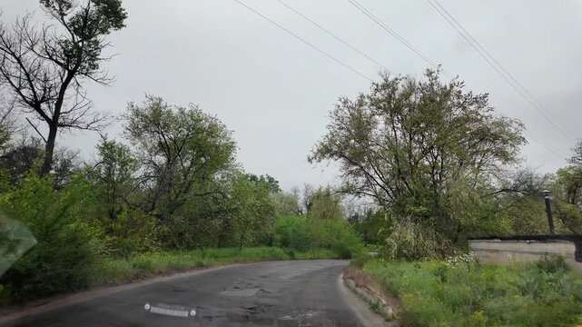 Slow-motion video shot from a moving silver car's perspective on a bumpy asphalt road in the countryside. The car's body 