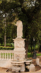 Obraz premium Ancient marble statue standing in the green gardens of Villa Borghese in Rome, Italy. The sculpture is surrounded by lush trees and soft natural light, creating an atmospheric scene of history and tim