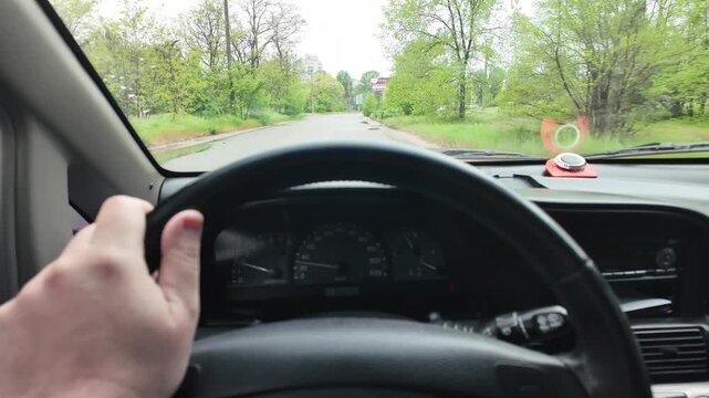 Slow-motion video shot from a moving silver car's perspective on a bumpy asphalt road in the countryside. The car's body 