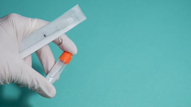 Close-up of gloved hand holding laboratory sample tube and sterile swab kit against blue background. Concept of DNA testing, medical diagnostics, laboratory research and healthcare analysis