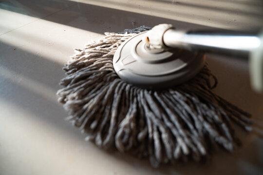 Close-up of a gray microfiber mop head resting on a tiled floor with sunlight casting shadows