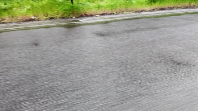Slow-motion video shot from a moving silver car's perspective on a bumpy asphalt road in the countryside. The car's body 