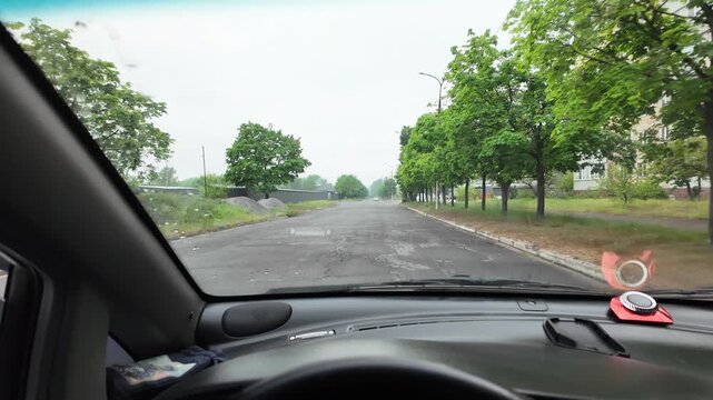 Slow-motion video shot from a moving silver car's perspective on a bumpy asphalt road in the countryside. The car's body 