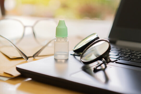Eyeglasses and eye drop bottle on laptop at desk workplace. Selective focus of eye drops