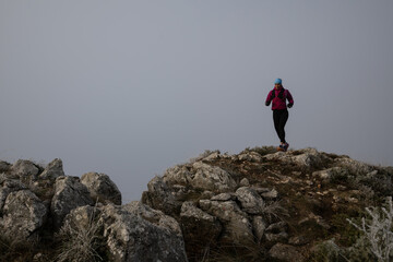 Obraz premium Woman Running On Rocky Mountain Trail In Foggy Weather For Outdoor Fitness And Adventure