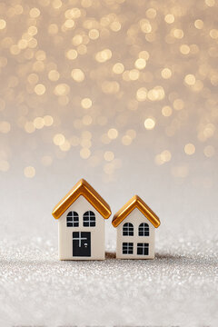 Two miniature houses with golden roofs against a shimmering bokeh background.