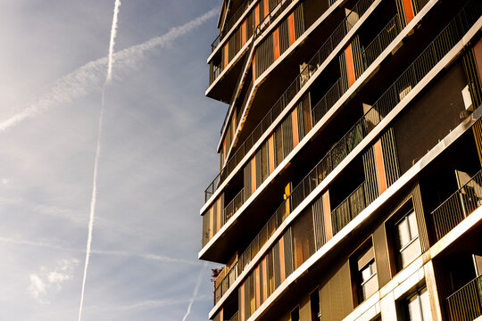 A Paris highrise in Rive Gauche catches sunlight along balcony edges, with residential windows rising into urban sky over the street below.