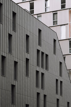 Muted gray facade detail in Rive Gauche, Paris, reveals narrow windows, vertical cladding and residential texture in close architectural view.