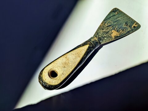 A neglected putty knife showing significant material fatigue. The stained metal blade and scratched handle of this painter's scraper demonstrate heavy industrial use and messy plaster residue