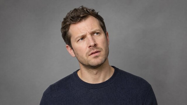 Confused Man Looking Up with Thoughtful Expression on Grey Background