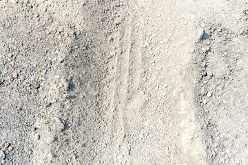 Fine, grainy material, gray sand, construction dust, or road base. Tire tracks are visible in the center. © Joshua Prasetyadi