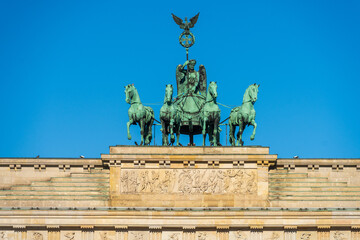 Naklejka premium Detail of the bronze quadriga sculpture on top of the Brandenburg Gate in Berlin against a clear blue sky.