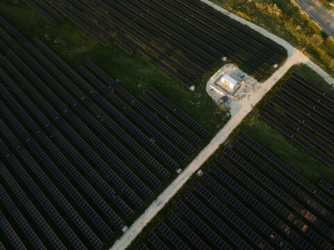 Aerial view of a solar panel farm with rows of photovoltaic modules and a small utility building under warm sunset light Augusta, Sicily, Italy.
