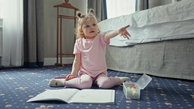Creative little girl with pigtails sitting on the floor drawing in a coloring book, then suddenly getting upset and emotional, yelling loudly before calming down and smiling