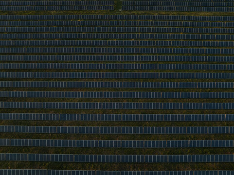 Aerial view of rows of solar panels in a large photovoltaic power plant on green fields Augusta, Sicily, Italy.