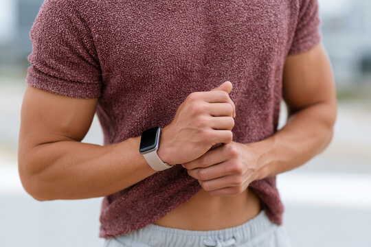 Athletic man checks smartwatch during outdoor activity. Focused on fitness, he monitors his pace or heart rate. Close-up highlights his determined posture and active lifestyle