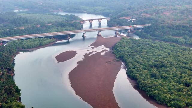 Cinematic aerial view of a winding river flowing through dense mangrove forests, with long bridges crossing above and exposed sandbanks creating organic patterns across the waterway.