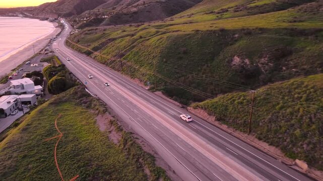 Coastal Sunset on PCH Pacific Coast Highway from Malibu hillside at sunset, California coast emerging as the camera passes lush green slopes at golden hour with beautiful pink skies.