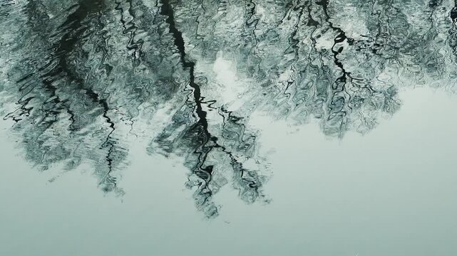 Dark rippled water surface with distorted black and white reflections, creating an abstract natural texture and moody background pattern.
