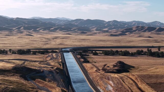 Water flowing through the deserts hills of the California Aqueduct canals. Wide landscape of agricultural man-made river delivering water to agricultural farmlands for irrigation in rural farmlands.