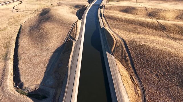 Water flowing through the California Aqueduct river canals. Wide landscape of agricultural man-made river delivering water to agricultural farmlands for irrigation in rural farmlands along I-5 Highway