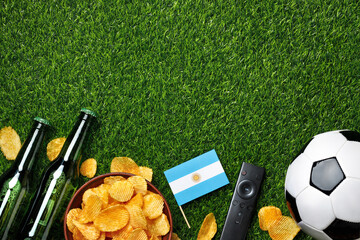 Naklejka premium A soccer balls, green beer bottles, potato chips and Argentine mini flag on green grass create the perfect game viewing atmosphere for Argentine fans. Top view with copy space.