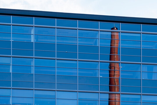 Blue glass catches reflection across a strict facade grid as a chimney cuts through windows on an industrial building exterior surface