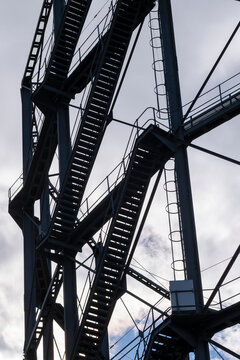 Steel staircase climbs through industrial framework as ladder, beams and metal shadow turn the vertical structure into graphic infrastructure